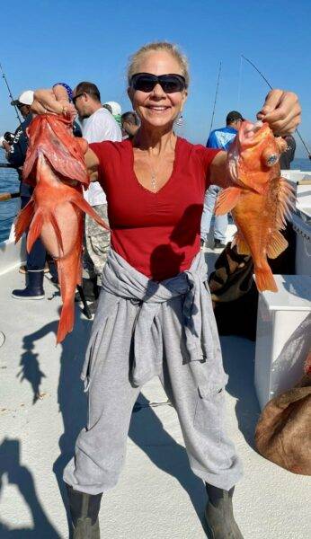 Smiling hot-chick proudly displaying two red fish caught during a sea excursion on a tropical cruise, exemplifying a unique onboard experience.