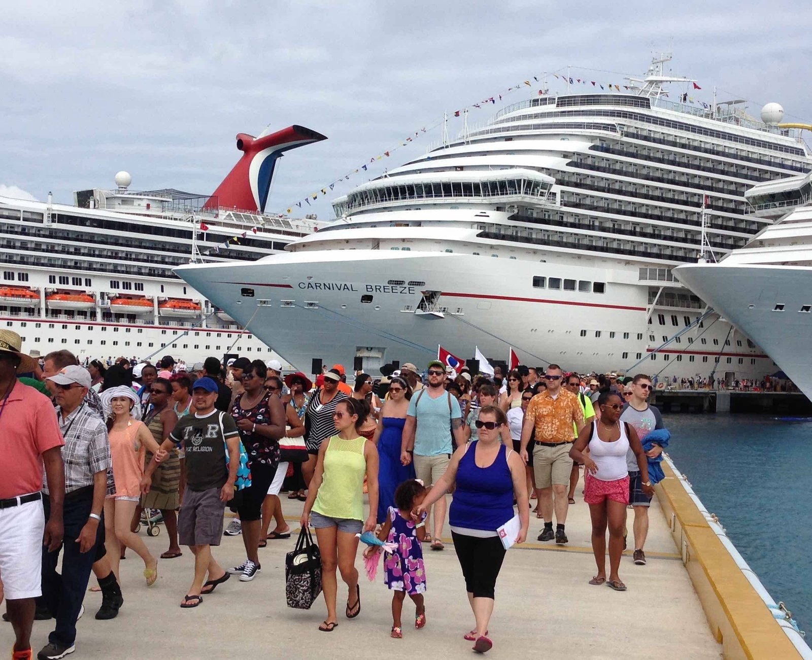Passengers on a sunny dock walking towards cruise ships for a group travel adventure, featuring ocean liners ready for Caribbean, Mediterranean, and Alaskan cruises.