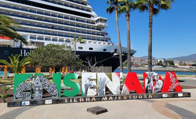 Colorful Ensenada sign with a large cruise ship docked in the background, set against a clear blue sky.