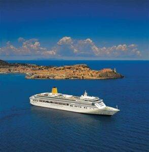 Cruise ship sailing near a scenic coastal town with a clear blue sky and calm waters.