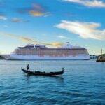 Large cruise ship docked near historic buildings in a scenic European port with a gondola in the foreground.