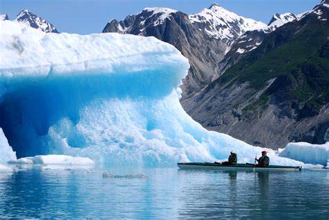 Kayakers near a massive glacier in Glacier Bay National Park, Alaska with snow-capped mountains in the background