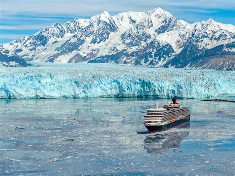 A luxury cruise ship sailing in front of a majestic glacier and snow-capped mountains in Alaska.