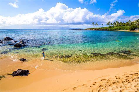 Sunny tropical beach with golden sand, turquoise water, and swimmers in the sea.