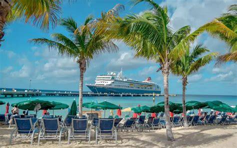 Cruise ship docked at a tropical beach in Turks and Caicos, with palm trees, beach chairs, and umbrellas under a bright blue sky.