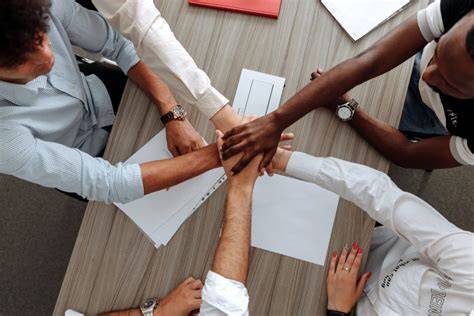 Group of diverse hands coming together in a show of unity over a table with documents.