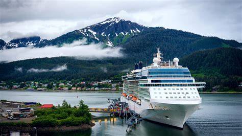 Luxury cruise ship docked in a scenic Alaskan port with snow-capped mountains in the background