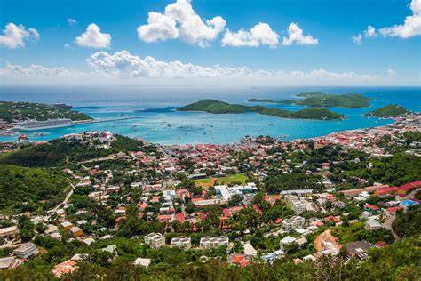 Aerial view of St. Thomas in the U.S. Virgin Islands, featuring lush green hills, vibrant buildings, and the turquoise waters of the Caribbean Sea with several small islands in the background.