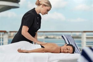 Woman enjoying a relaxing massage on the deck of a luxury cruise ship with ocean views in the background.