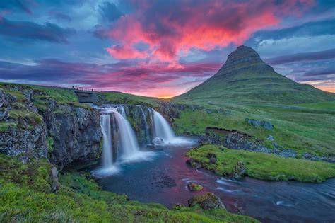 Breathtaking waterfall flowing into a serene river with a mountain and vibrant sunset sky in the background