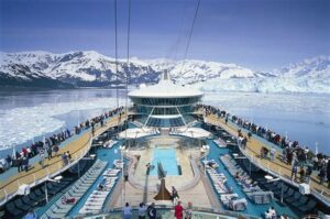 Cruise ship deck with passengers enjoying stunning views of Alaskan glaciers and snowy mountains.