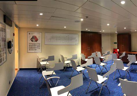 Empty conference room on a cruise ship with white chairs and blue carpet.