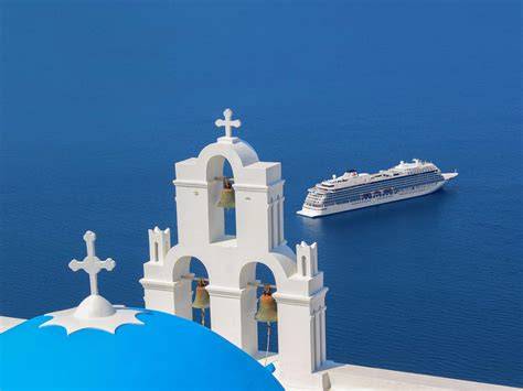 A cruise ship sailing near the iconic blue-domed churches of Santorini, Greece, with the deep blue Aegean Sea in the background.