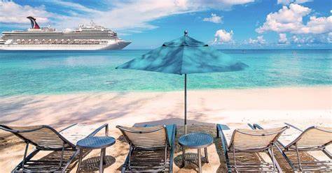 Beach chairs and umbrella on a tropical beach with a cruise ship in the background.