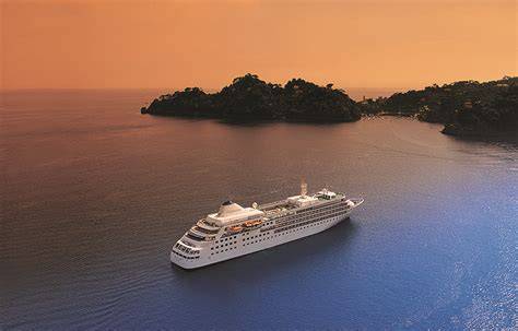 A cruise ship sailing near a lush tropical island at sunset, with a serene and picturesque view.