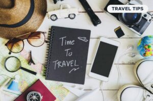 Travel essentials including a hat, sunglasses, a camera, a smartphone, a map, and a notebook with "Time To Travel" written on it