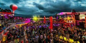 Large crowd enjoying a colorful nighttime event on a cruise ship deck