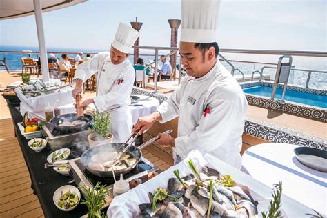 Chefs preparing gourmet seafood on the deck of a luxury cruise ship with the ocean in the background.