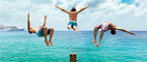 Three friends jumping into the ocean with a cruise ship in the background.