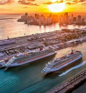 Two cruise ships departing from a port at sunset with a city skyline in the background.