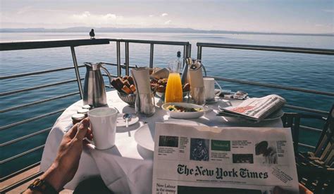 Breakfast on a cruise ship balcony with a stunning ocean view, featuring coffee, juice, pastries, and a newspaper.