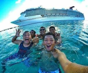 Group of friends enjoying a swim in the ocean with a cruise ship in the background.