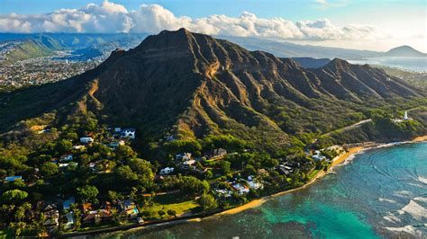 Aerial view of a coastal town with lush greenery and a towering mountain backdrop.