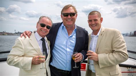 Three men in suits enjoying drinks on a cruise ship, smiling and posing together.