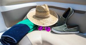 Beach essentials including a hat, sunglasses, towel, and shoes on a boat seat.