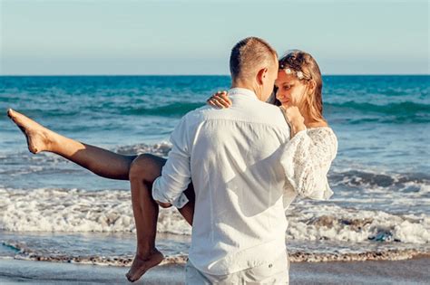 Romantic couple on a beach with the man carrying the woman by the ocean during a tropical getaway.