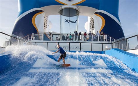 Man surfing on a flow rider onboard a cruise ship with a skydiving simulator in the background