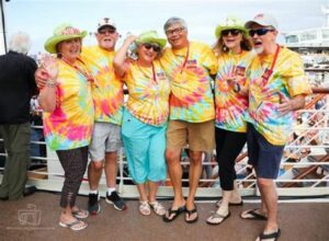 Group of seniors in colorful tie-dye shirts enjoying a themed cruise onboard a ship.