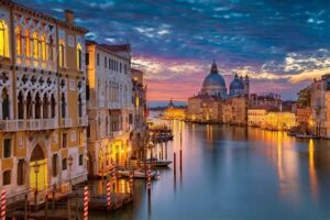 Stunning sunset over the Grand Canal in Venice, Italy, with historic buildings illuminated.