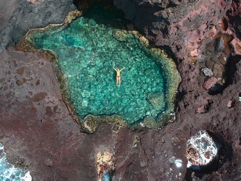 A person floating in a natural turquoise rock pool surrounded by rugged volcanic rocks.