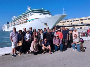 Group of people posing for a photo in front of a cruise ship at a port