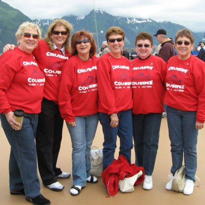 Group of friends enjoying their cruise vacation in Alaska, wearing matching red 'Cruise Cousins' sweatshirts, showcasing the joy of group travel and shared experiences.