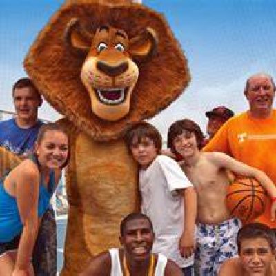 Joyful group playing basketball with an animated lion character on a cruise ship deck under a clear sky.